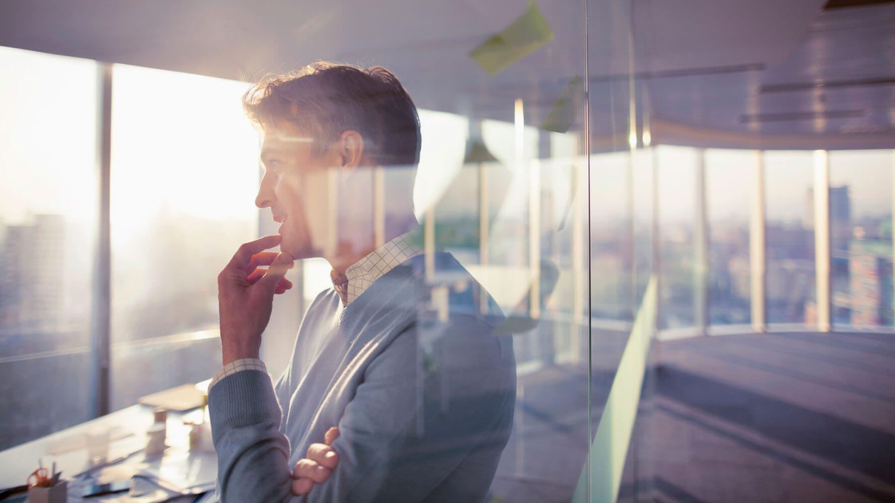 Rethinking your income strategy, a man in an office building stands nearby a window pondering the future.