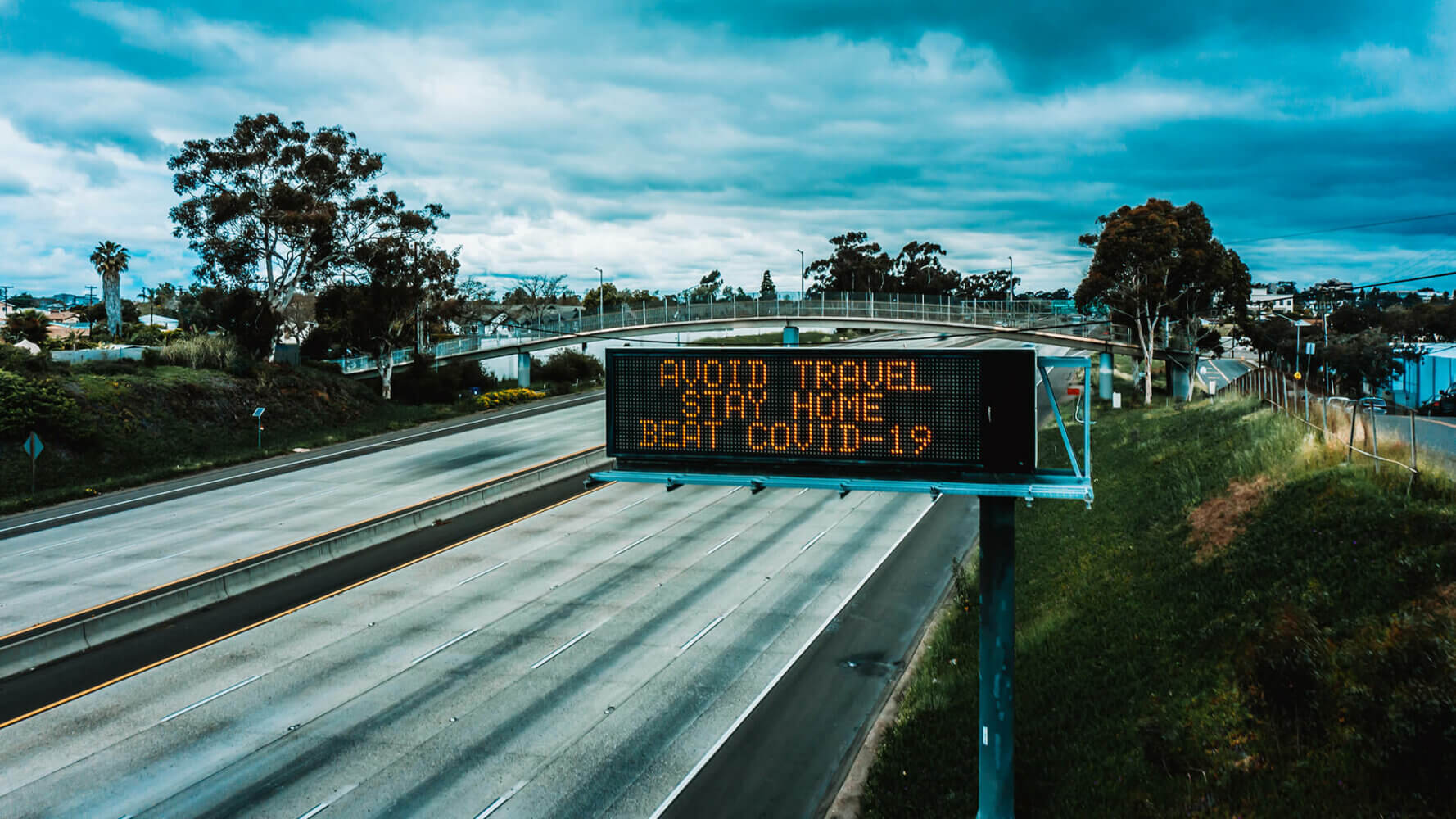 A sign above the freeway states the ominous words "AVOID TRAVEL STAY HOME BEAT COVID-19"