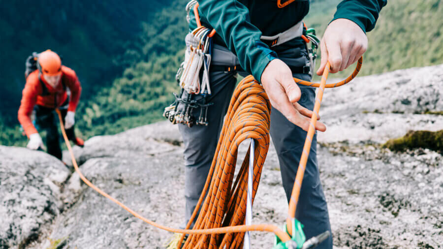 Managing risk is shown as two climbers use safety rope to pull themselves up a cliff face.