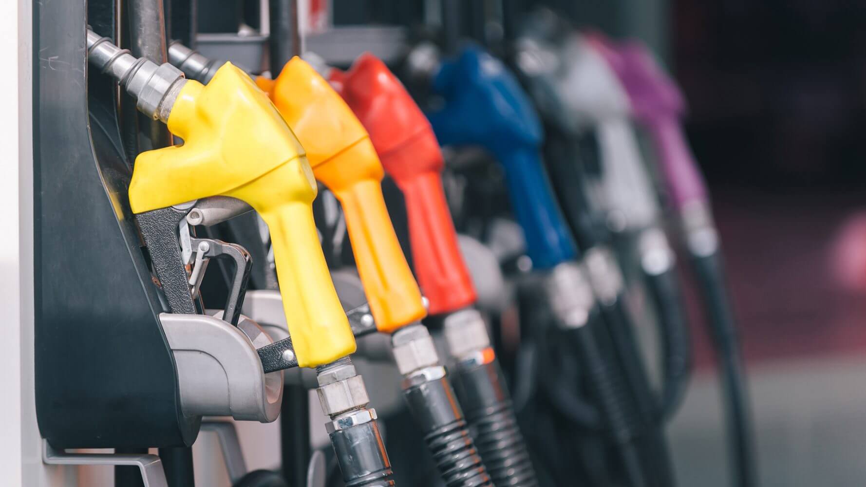 Considering high inflation, what can be done to mitigate these high costs? Gas fuel dispensers lie in a row, each in a different bright color.