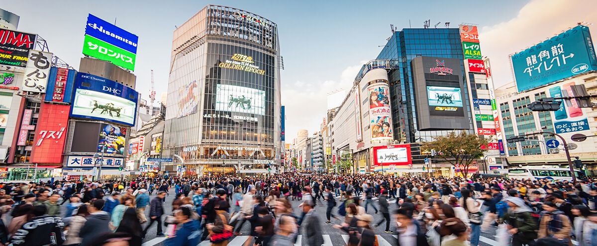 Panorama Shot of People crossing the crowded famous Shibuya Crossing in Downtown Tokyo, illuminated Shibuya Buildings with billboards in the background. Twilight light, close to sunset. Shibuya Crossing, Shibuya Ward, Tokyo, Japan, Asia.