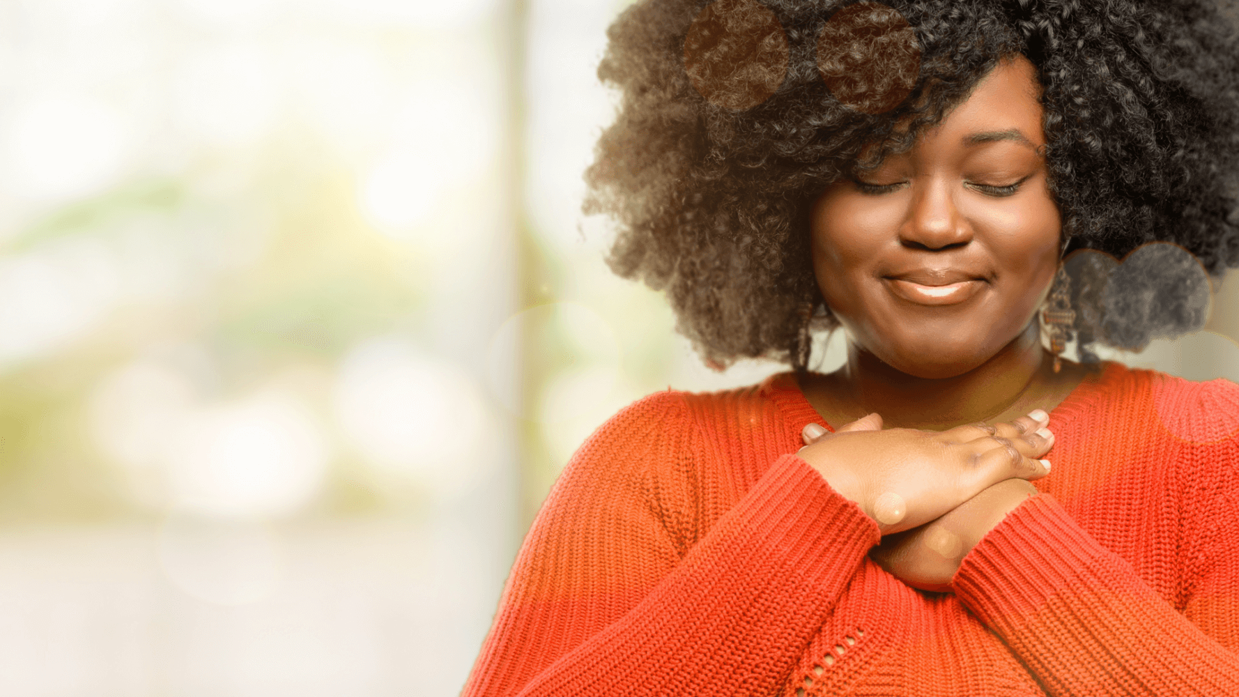 Woman in bright orange sweater thinks deeply with eyes closed.