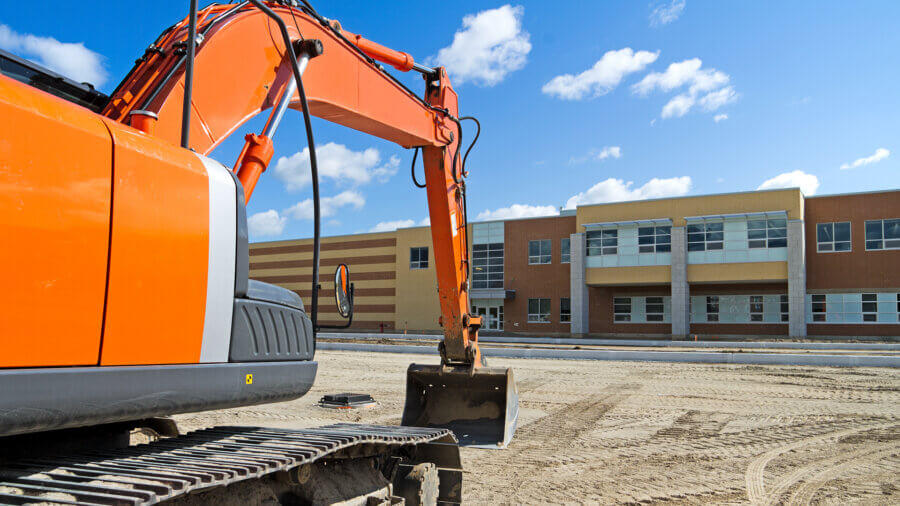 A bright orange construction excavator in the recently graded parking lot of a new high school.