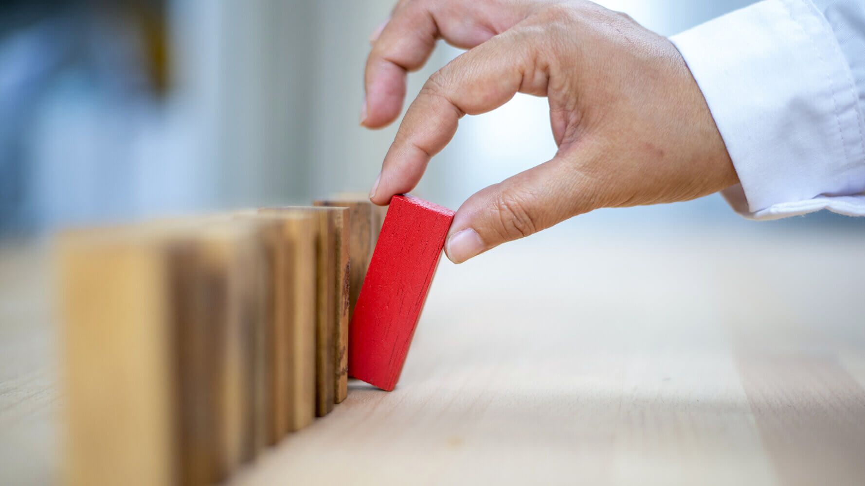 Man removing red domino from a line. Signifies the recognition and management of risk.