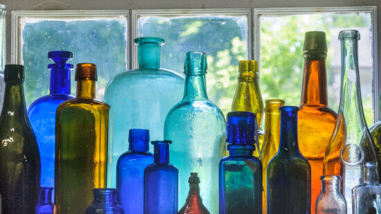 A collection of antique glass bottles in a dusty shop window in the Hudson River Valley of New York.