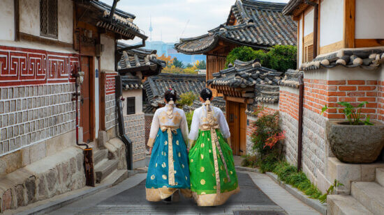 Back of two woman wearing hanbok walking through the traditional style houses of Bukchon Hanok Village in Seoul, South Korea.