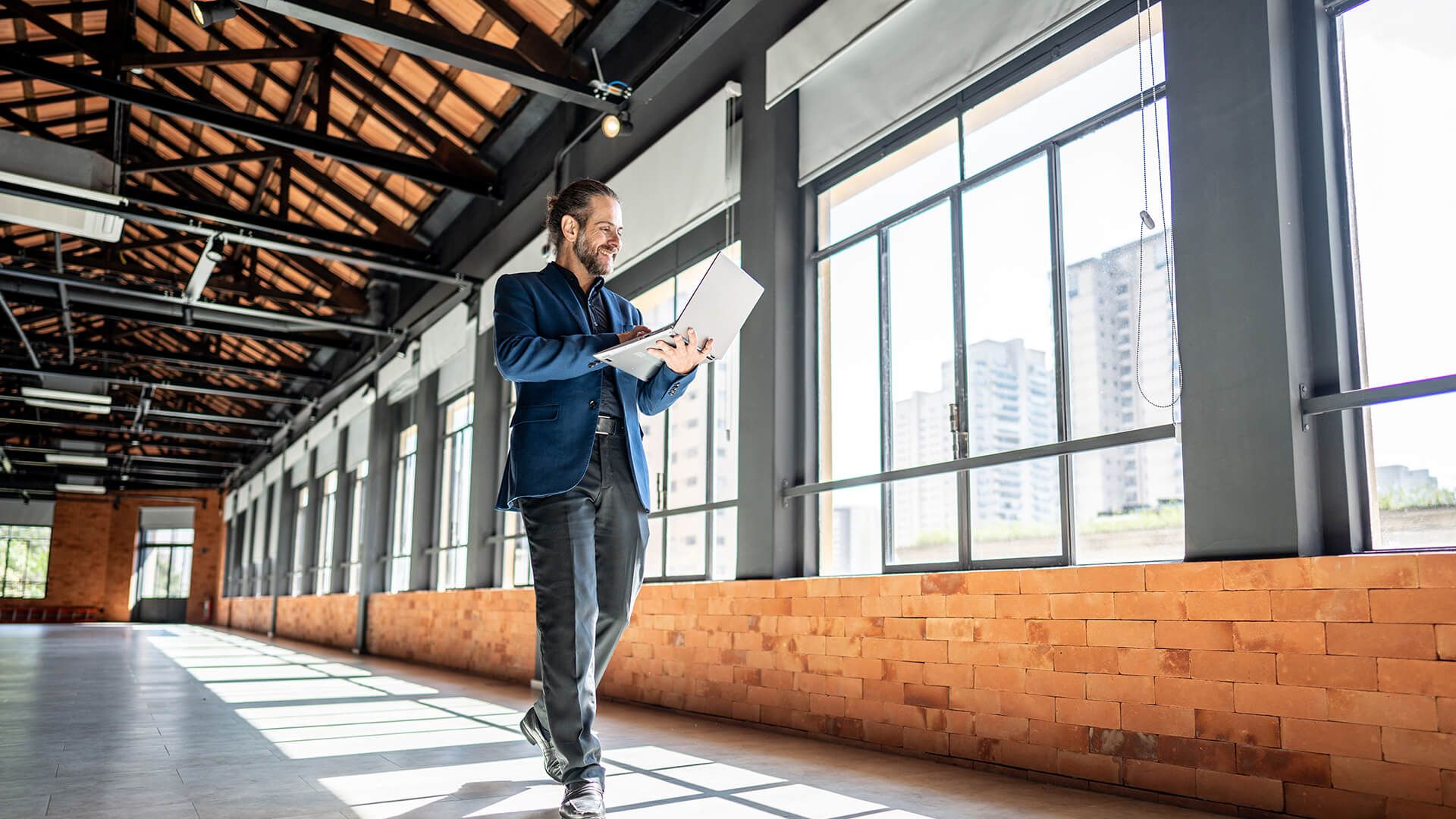 Man smiles as he walks through an office space with his laptop open