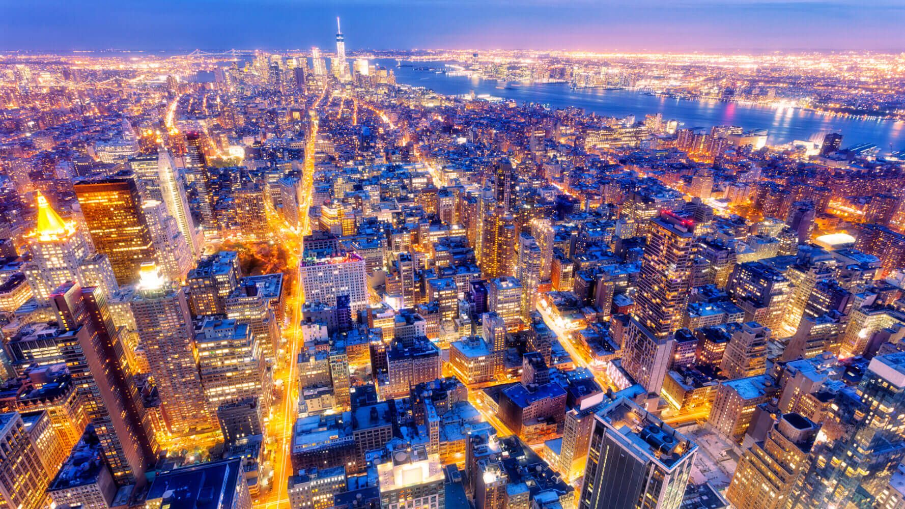 New York skyscrapers illuminated at dusk, the Fifth Avenue and other streets with traffic are visible as orange vibrant lines. On the horizont can be seen a new One World Trade Center also known as Freedom Tower. Midtown Manhattan, elevated view, horizontal orientation, USA.