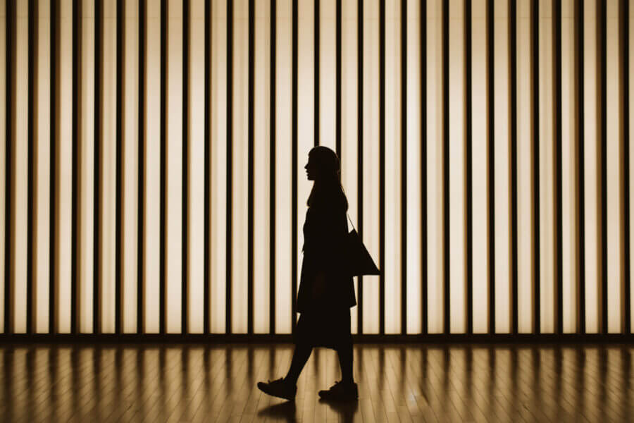 Silhouette of woman walking in front of striped illuminated wall