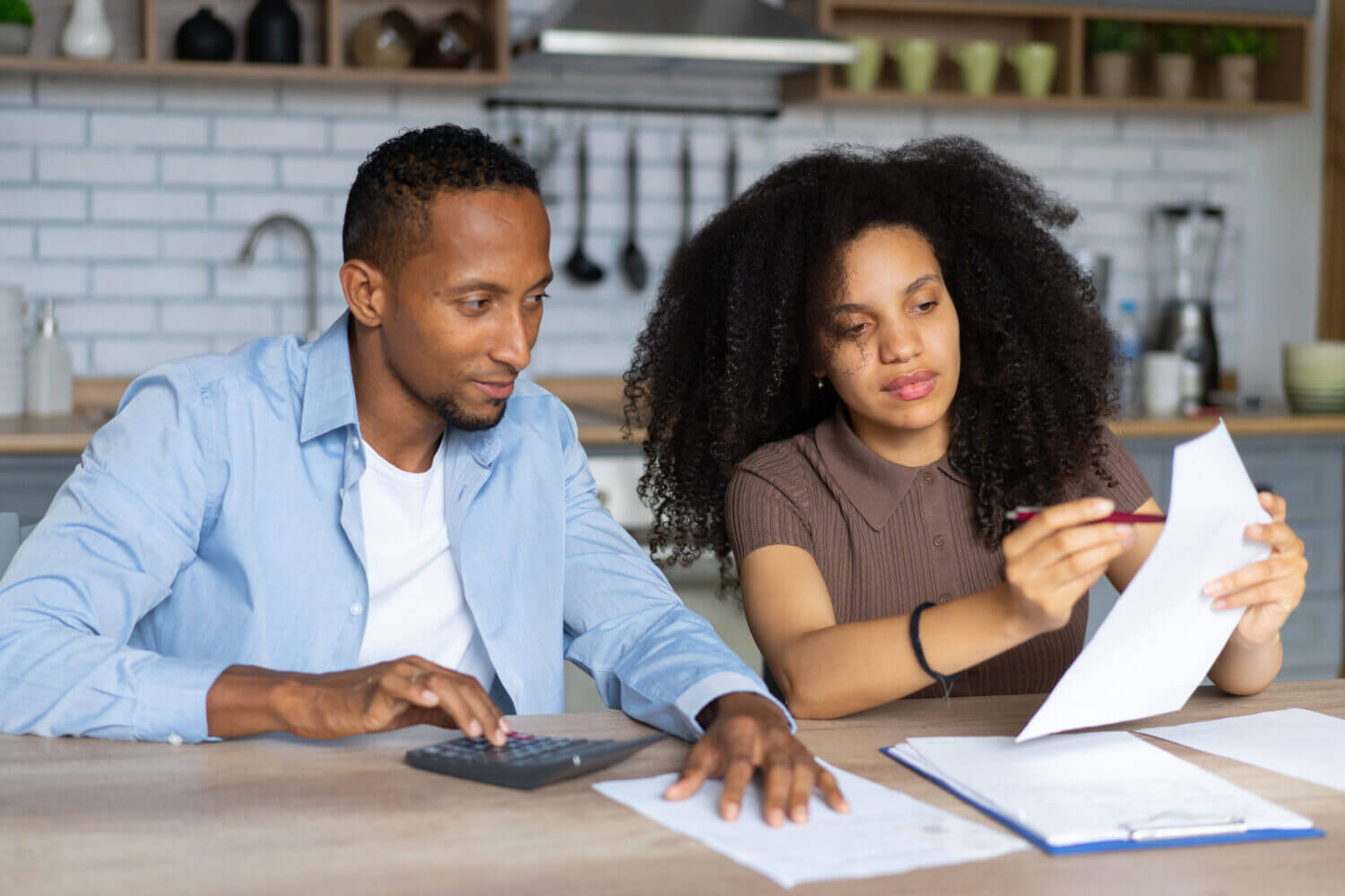 A couple are working together to calculate their monthly spending and income while worrying about the high cost of living, sitting together at a kitchen table