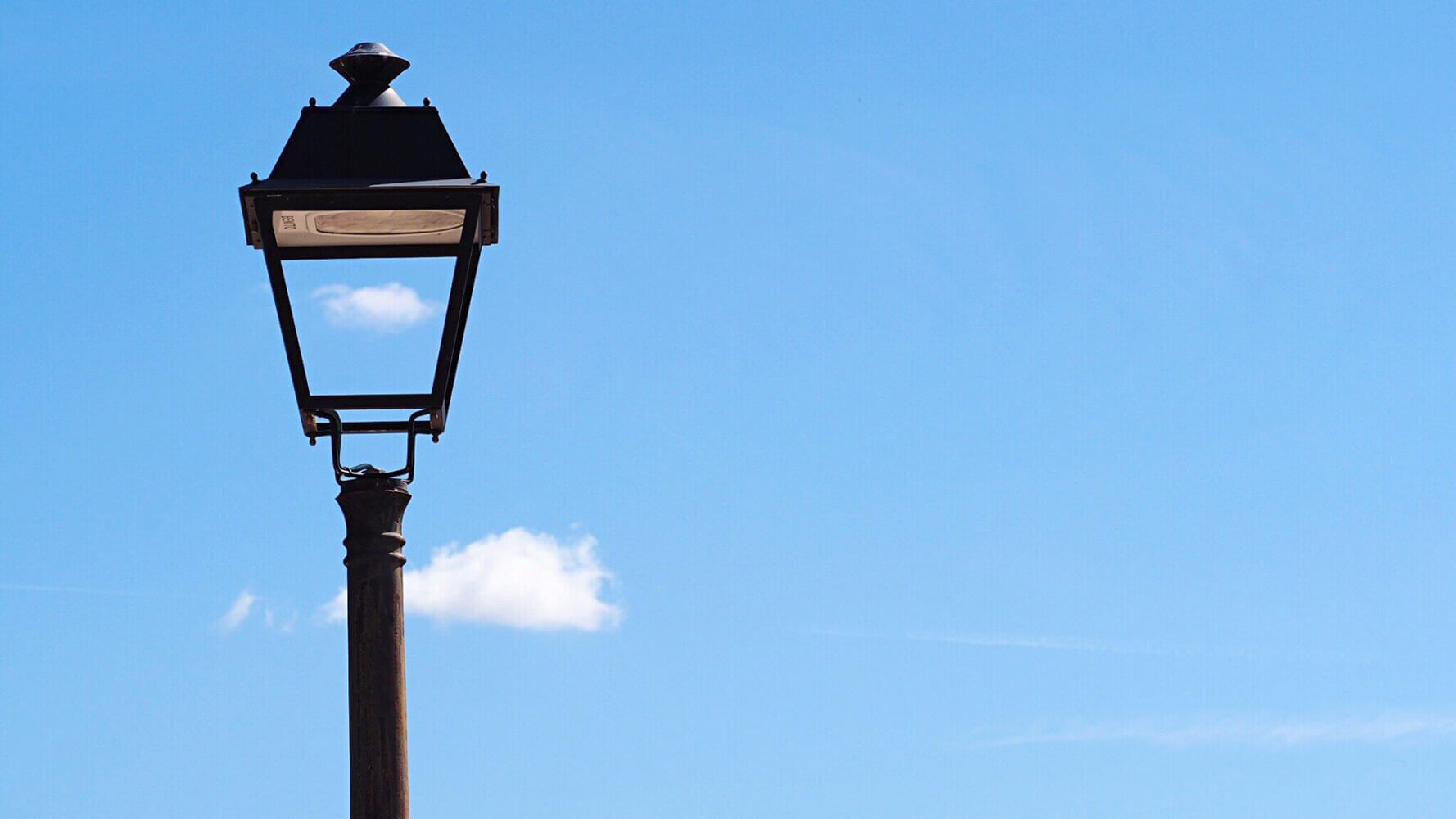 Low Angle View Of Bird Perching On Street Light Against Blue Sky