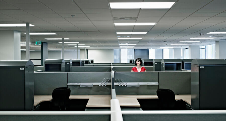 Businesswoman standing alone at cubicle in empty office contemplating commercial real estate as an opportunity.