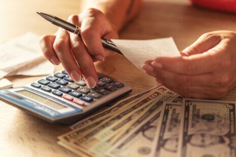 Entrepreneur holds paper and does finances using calculator with money on the table