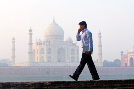 Businessman on a call walks along a ridge in front of the Taj Mahal.
