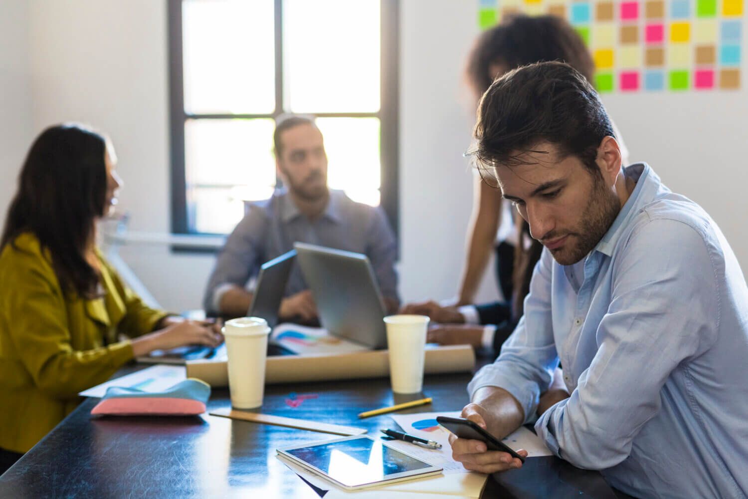 Man sits at a table during a meeting and checks the news on his phone.