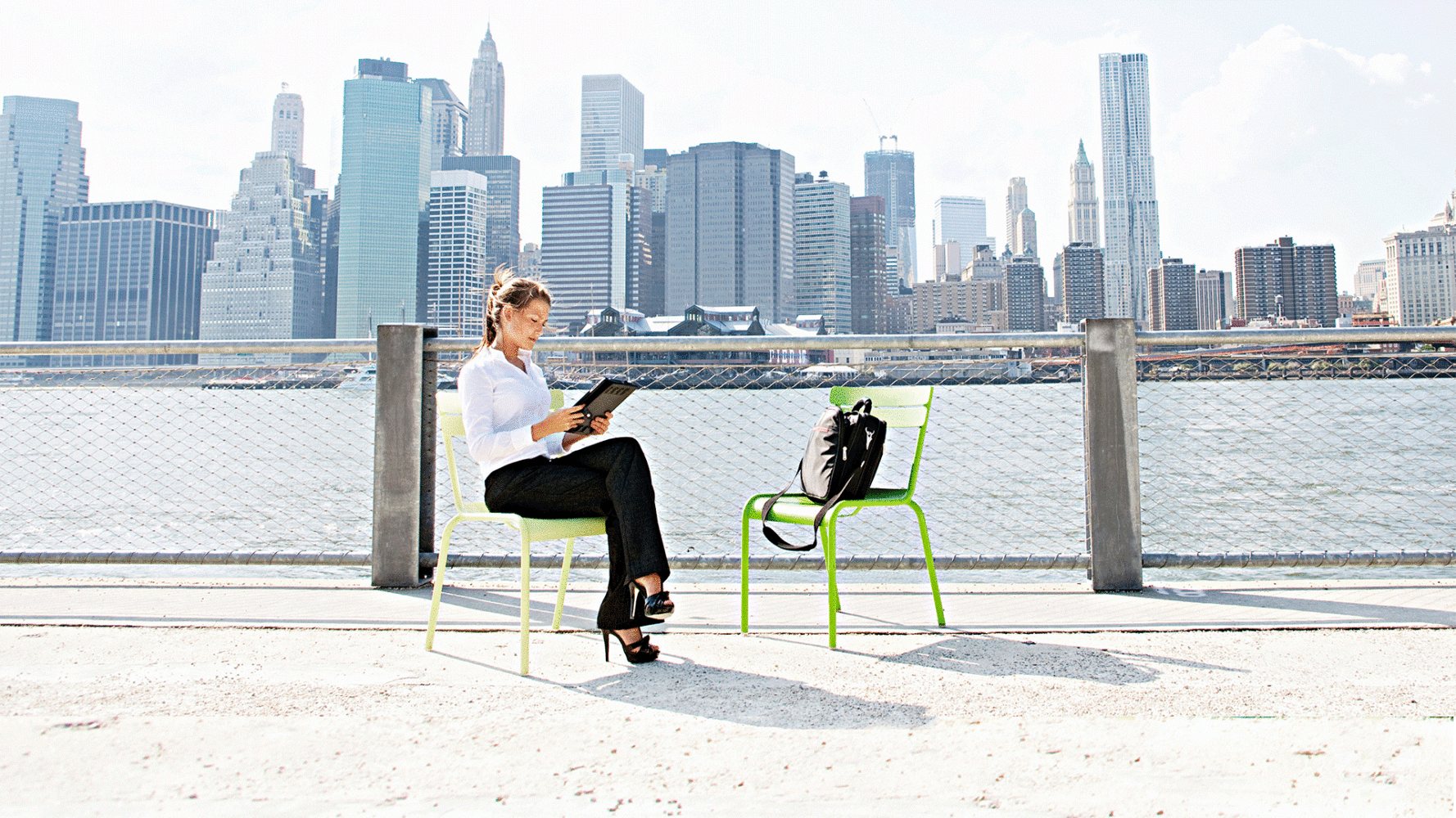 Woman sits with the NYC skyline in the background reading from her iPad.