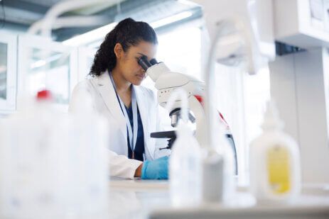 Woman in a lab looking into her microscope at her experiment.